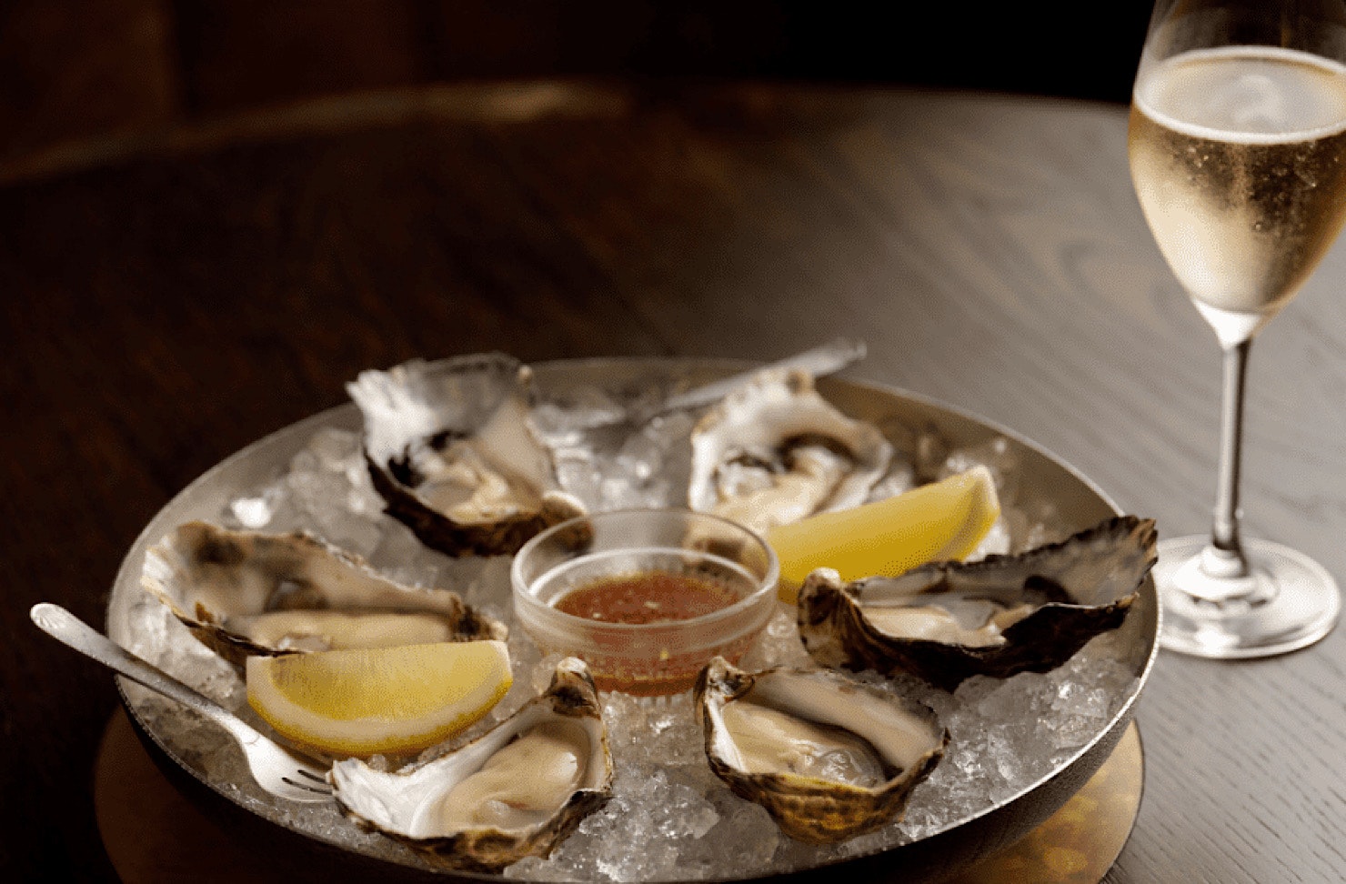 A silver platter of oysters, lemon and a glass of bubbles. 