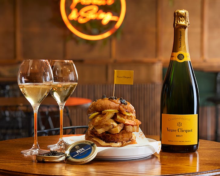 A stacked burger between a glass and a bottle of Veuve Clicquot. 