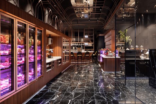 The inside of the butcher with marble floors, black ceiling, and a fridge with various cuts of meat.