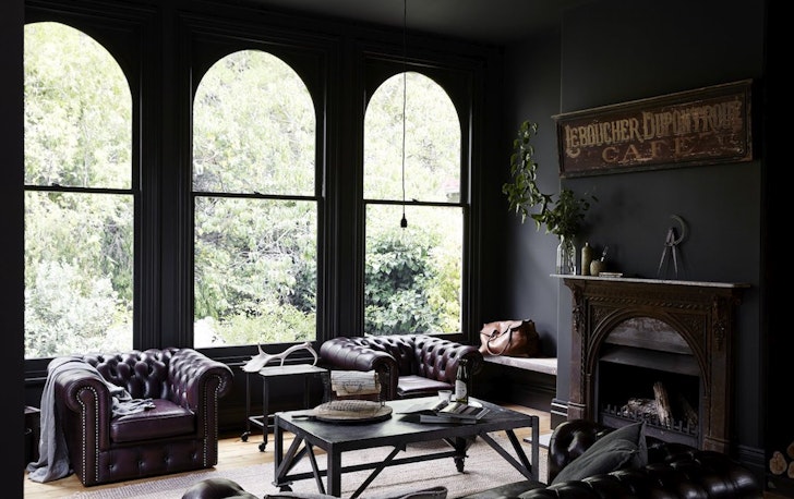 Three floor-to-ceiling windows with arched top are in a lounge room with two leather couch chairs and a fireplace.