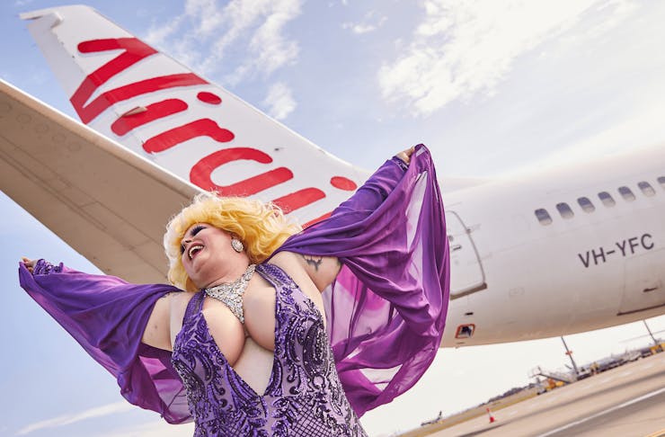 A person in a colourful purple outfit dancing in front of a plane.
