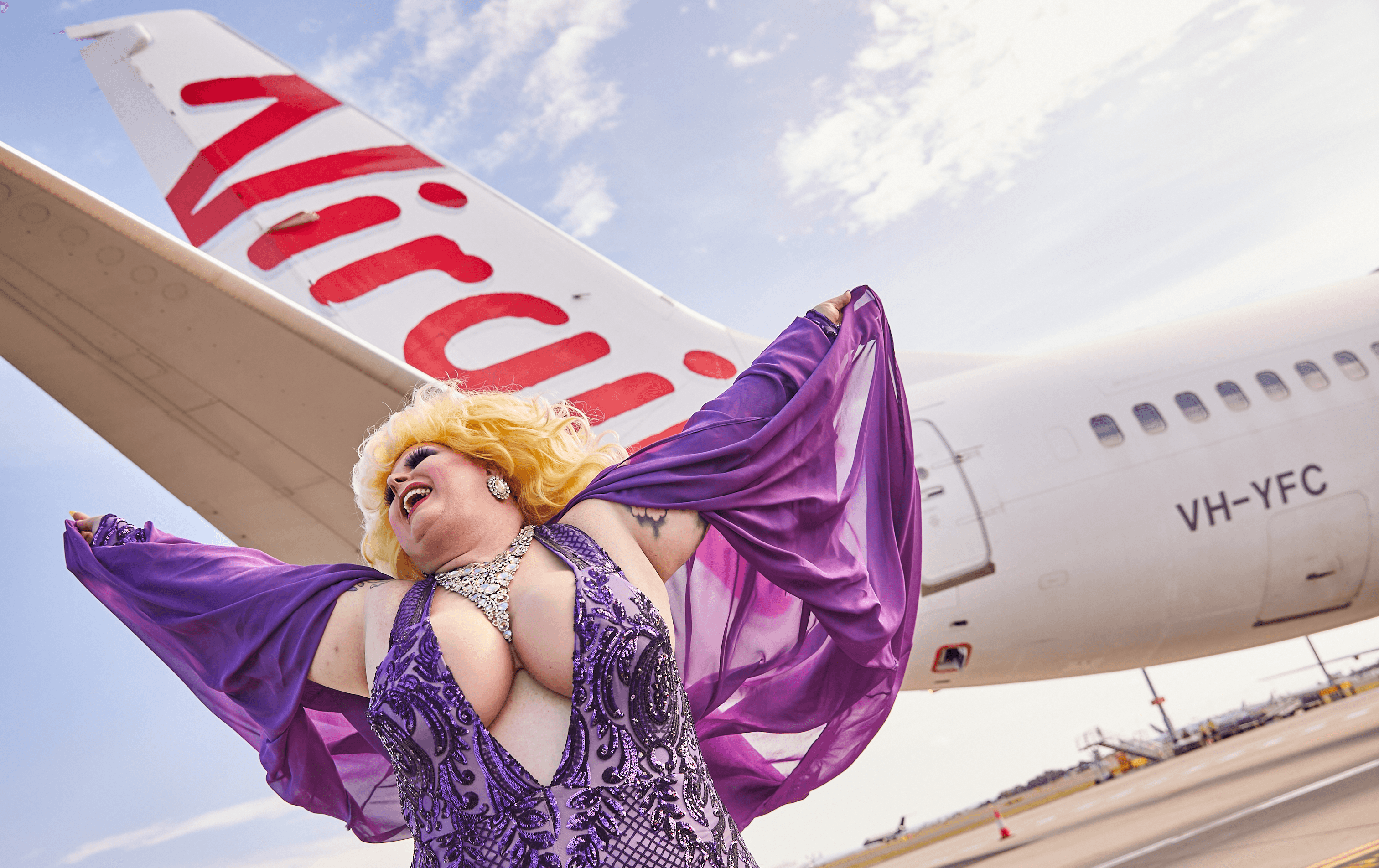 A person in a colourful purple outfit dancing in front of a plane.