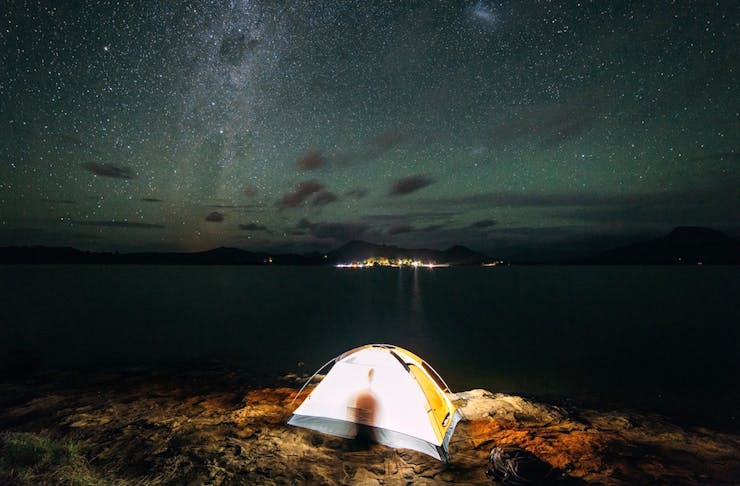 A small tent is set up beside a lake beneath a canopy of stars.
