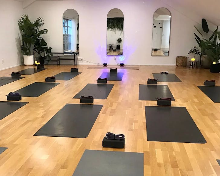 A minimalist yoga studio with three long wall mirrors, some plants, candles and yoga mats. 