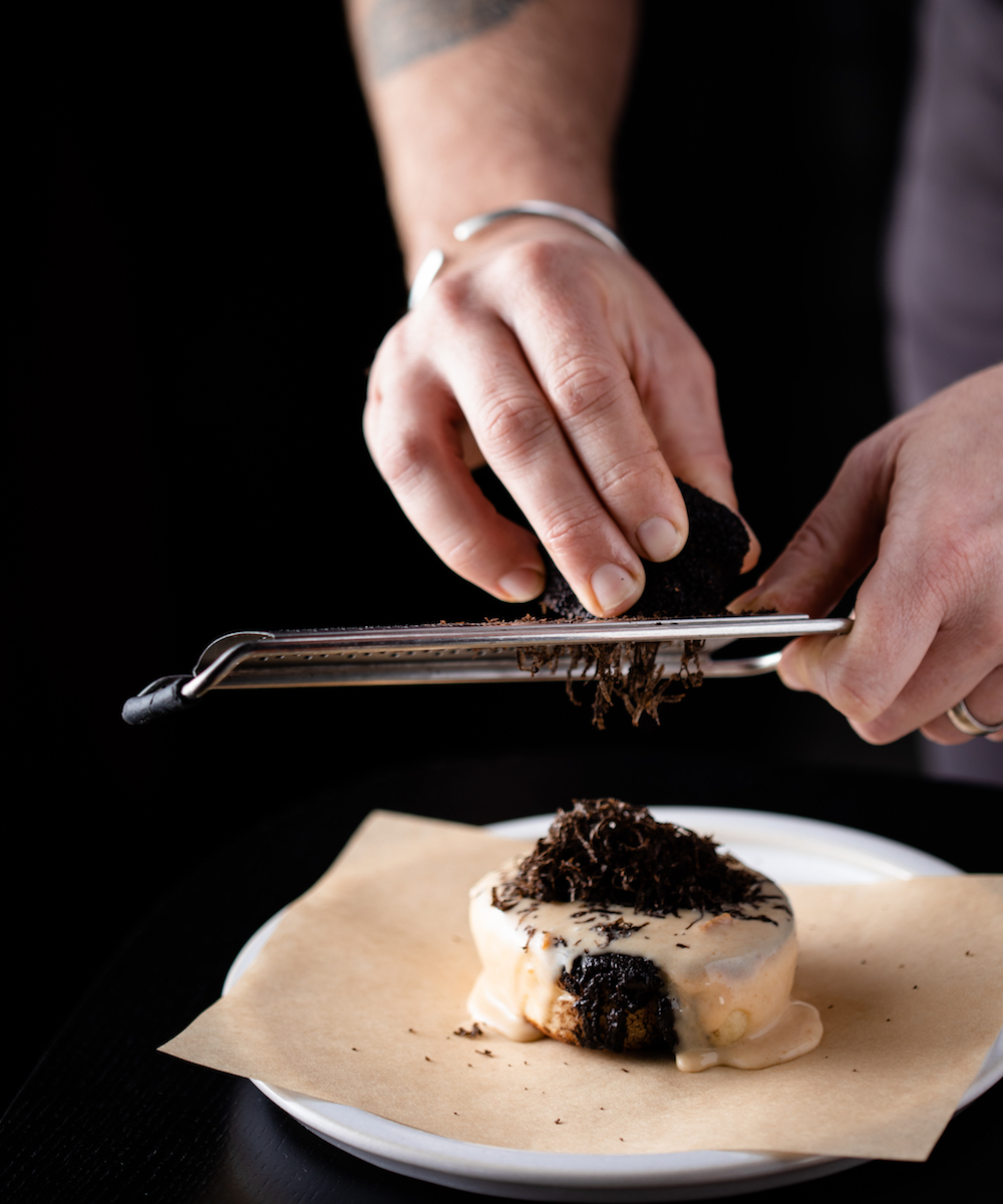 chef grates truffle onto a piece of gooey cheese