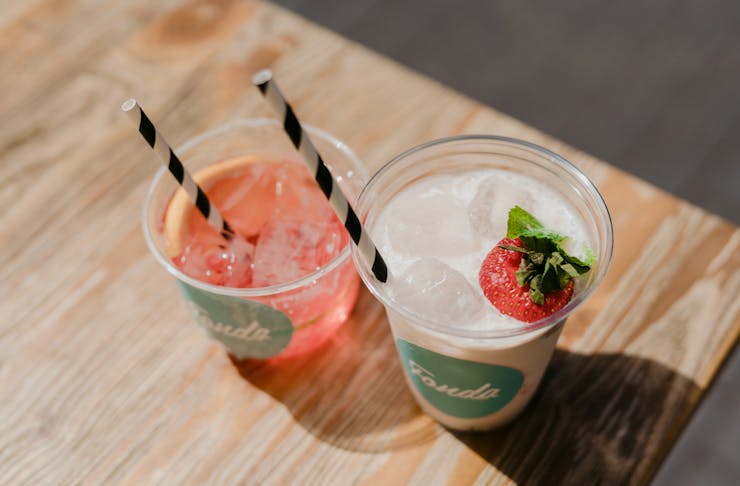 Two frozen cocktails each in a cup with a straw and garnished with a strawberry.
