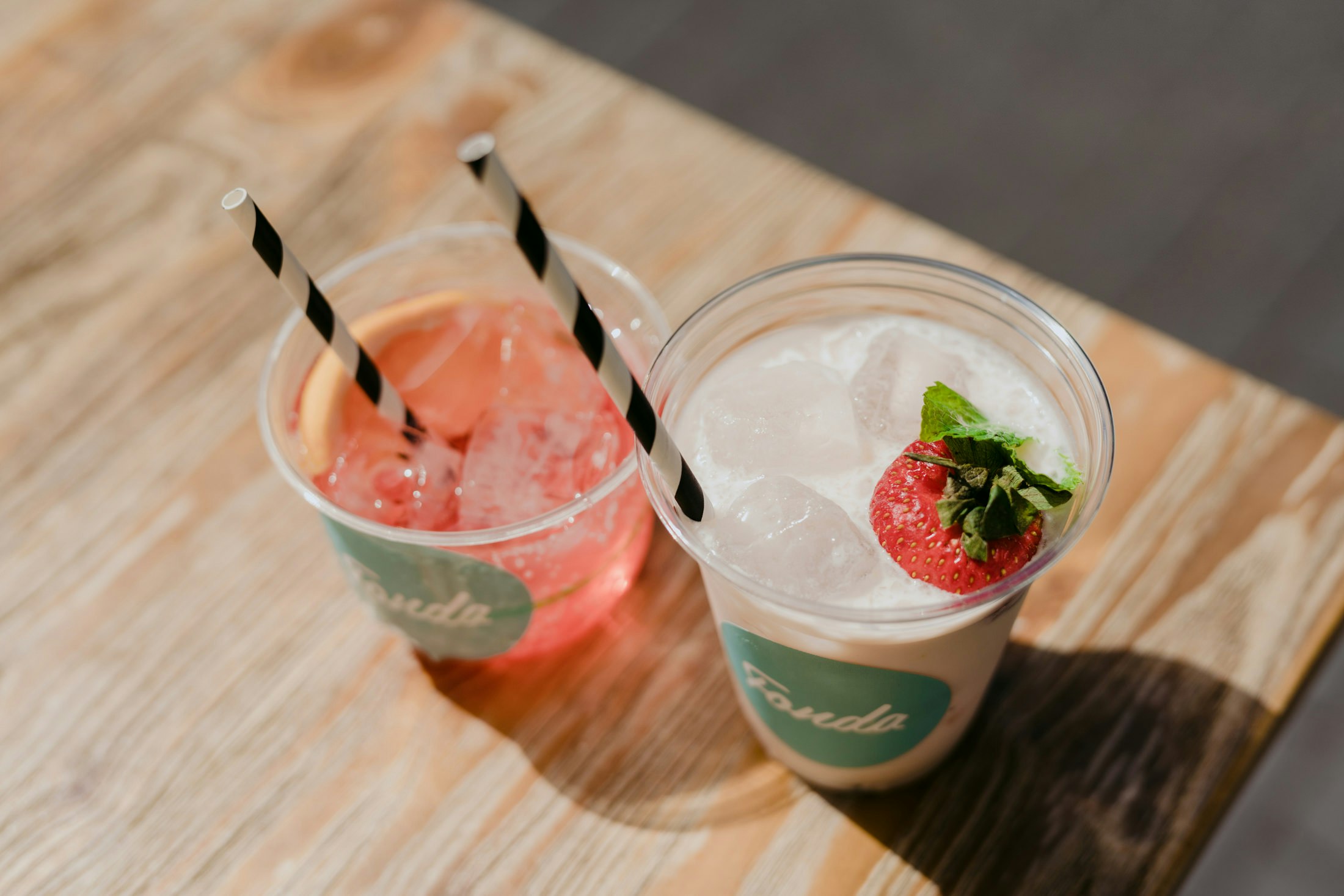 Two frozen cocktails each in a cup with a straw and garnished with a strawberry.