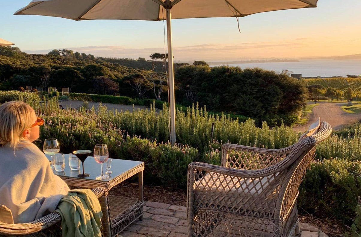 Girl sits at table during sunset and looks out on Waiheke Island