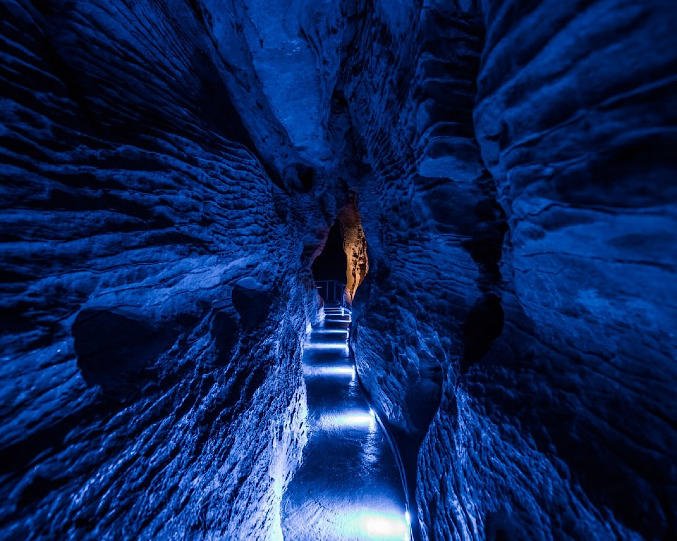 A narrow pathway through a cave is lit with blue light. 