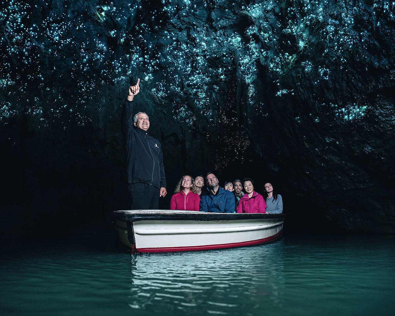 People sit on a boat and gaze up at the glow worms