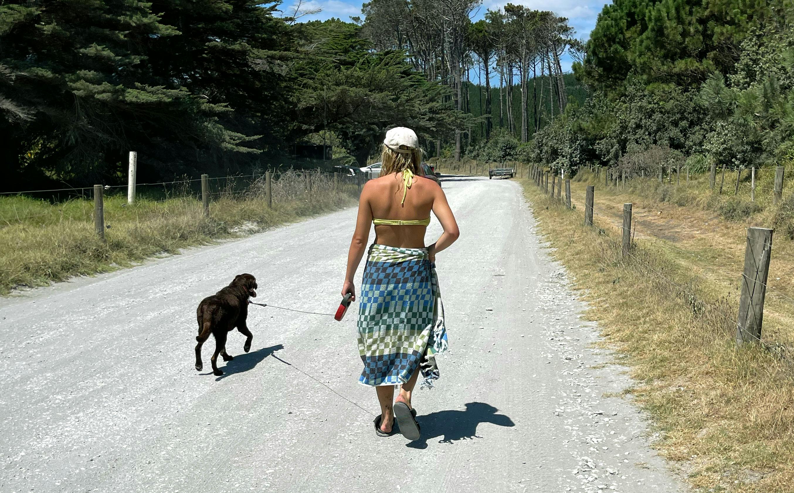 Woman walking her dog along a gravel road in summer