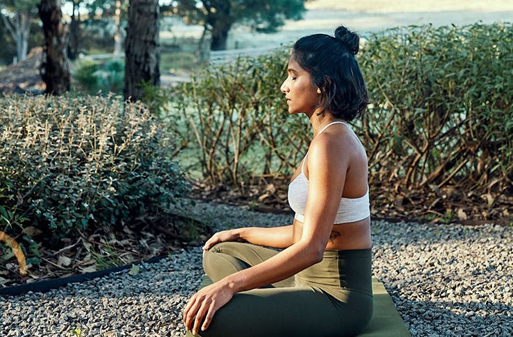 side profile of a woman meditating on a yoga mat outdoors. 
