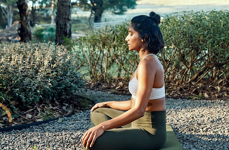 side profile of a woman meditating on a yoga mat outdoors. 