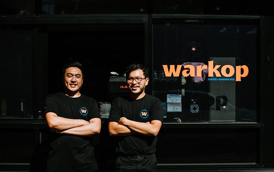 Two people with their arms crossed out front of a shop. 