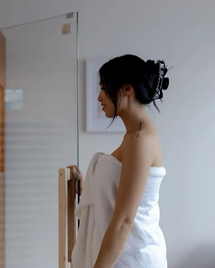 A woman in a towel goes to step into a private infrared sauna.