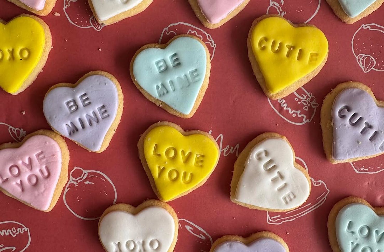 A collection of heart-shaped sugar cookies in pastel colours with cute lovely dovey words stamped into their icing. 