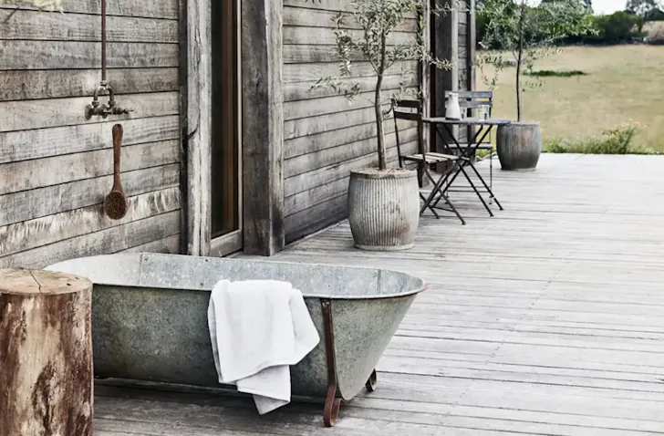 A rustic-style bath sits outside on a timber decking with a white towel hanging over the side.