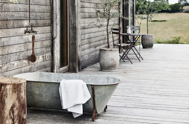 A rustic-style bath sits outside on a timber decking with a white towel hanging over the side.