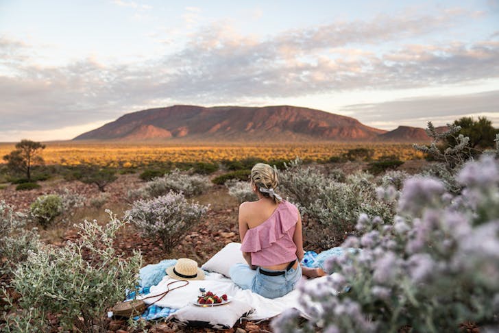 A woman sits on a picnic blanket as she gazes out towards the Western Australian outback.