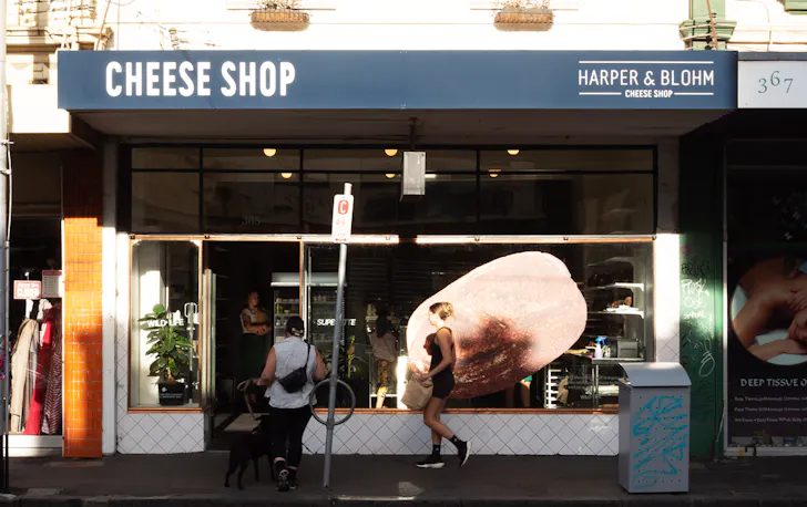 The outside of a store with the sun shining and people walking past.