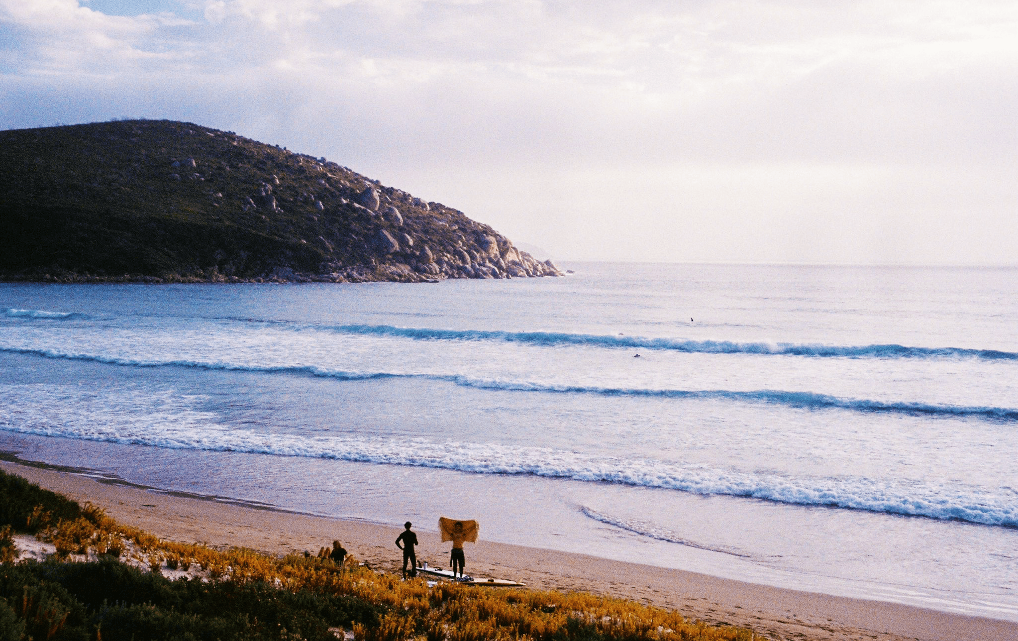 Small waves peeling and two people on the beach next to surfboards at one of the best beaches in Victoria.