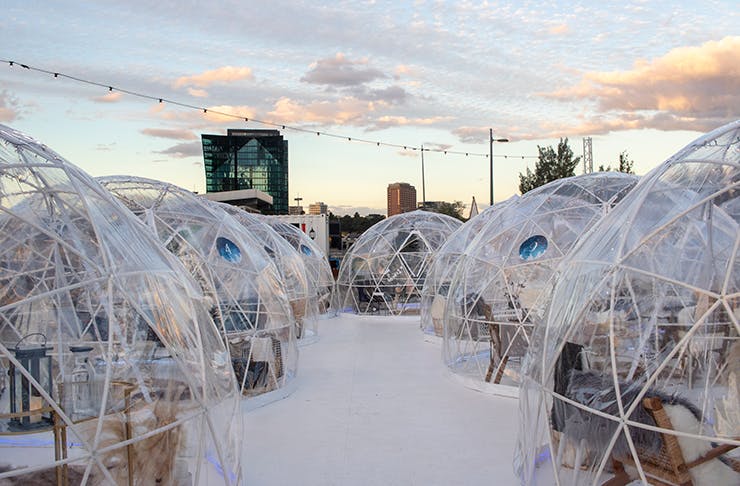 A cluster of see-through igloo's with fake snow on the ground with a sunset background 
