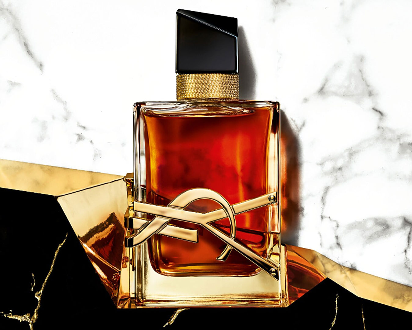 A dark amber perfume in a glass bottle with 'YSL' in gold on the side in front of a marble backdrop.