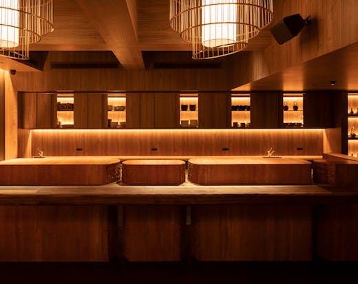 A wooden bar with dining stools and lights behind it. 