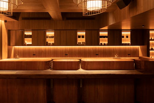 A wooden bar with dining stools and lights behind it.