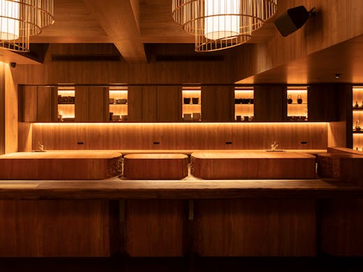 A wooden bar with dining stools and lights behind it. 