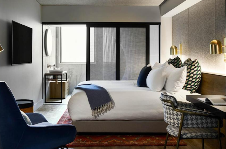A double bed sits in the middle of a pet friendly hotel in melbourne with a blue throw over.
