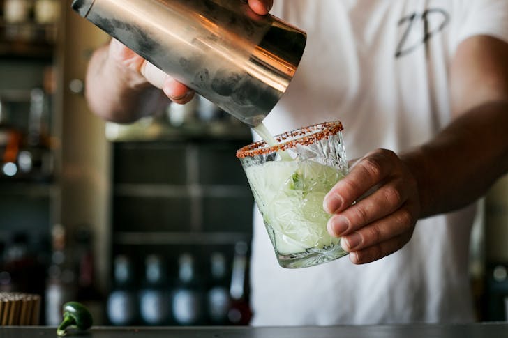 someone pouring a cocktail out of a stainless steel shaker