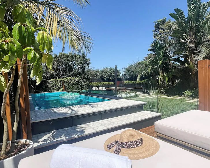 A nicely landscaped backyard with palm fronds and a modern swimming rectangular swimming pool with a jacuzzi.