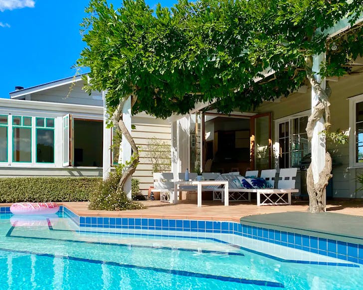 A house with a pool, patio furniture, and a vine-covered pergola.
