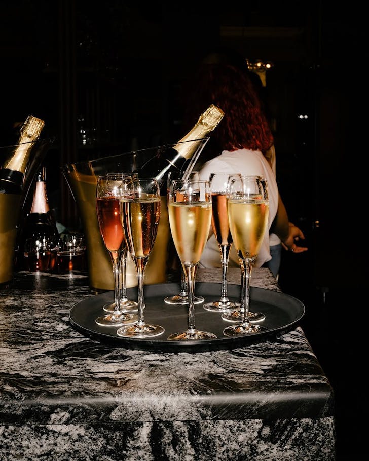 Glasses of champagne sit on a marble table in front of unopened champagne on ice.