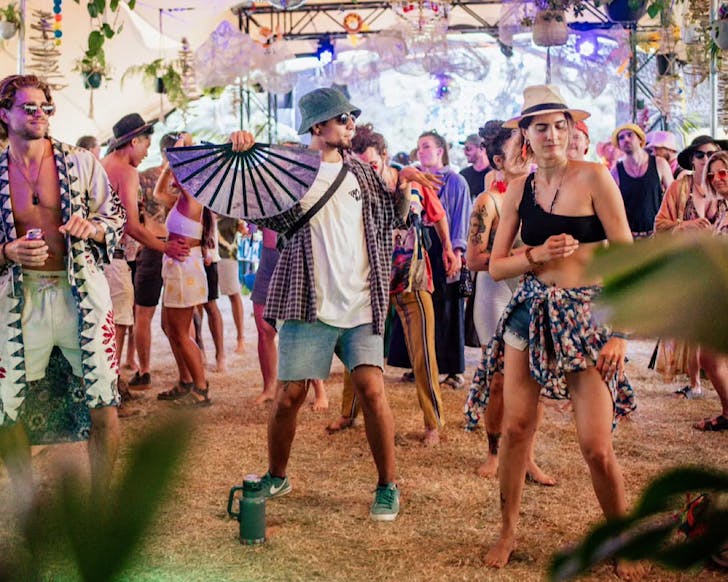 Colourfully dressed AUM festival goers groove on the grass in a tent-enclosed dancefloor.