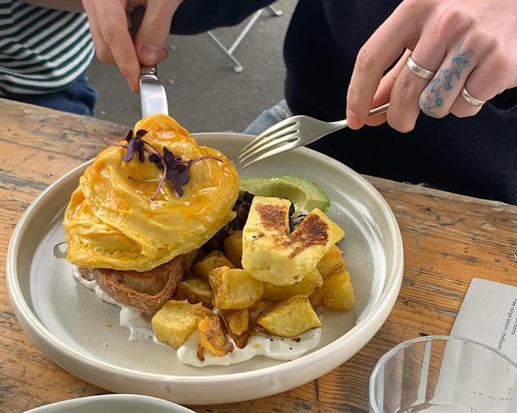 Closeup of someone holding their knife and fork, ready to eat beautifully yellow folded eggs on toast at Honey Bones.