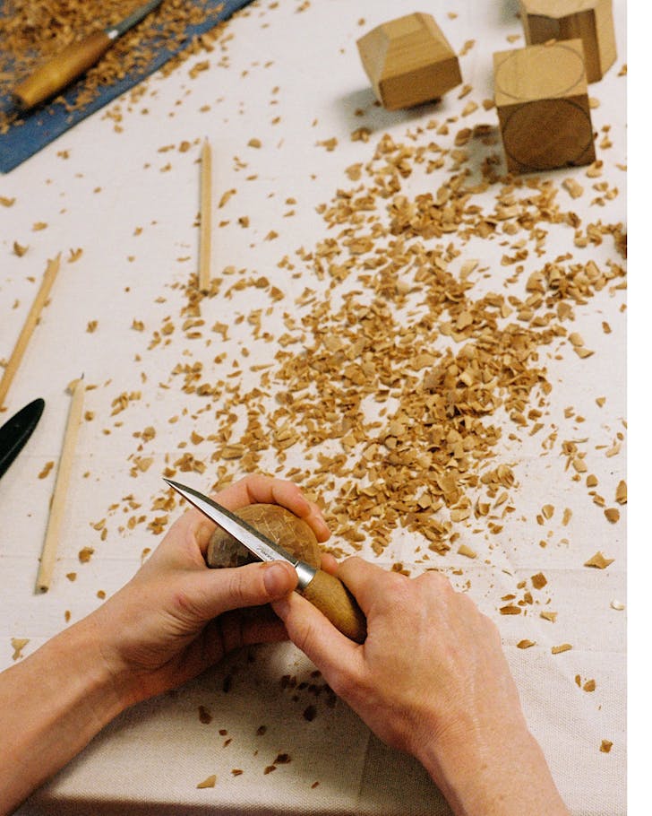 A woodworker turns blocks of wood into smooth spheres by hand.