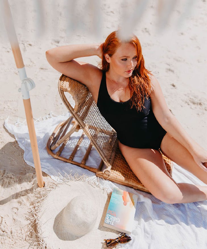 a woman lying on the beach in a black one piece