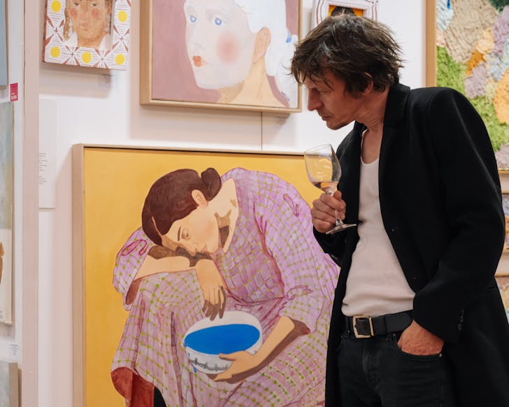 A man views works at the Affordable Art Fair, glass of wine in hand. 