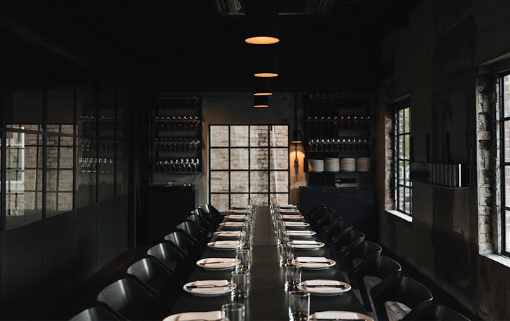 a dark room with a long table inside, and wine bottles on the wall at the end