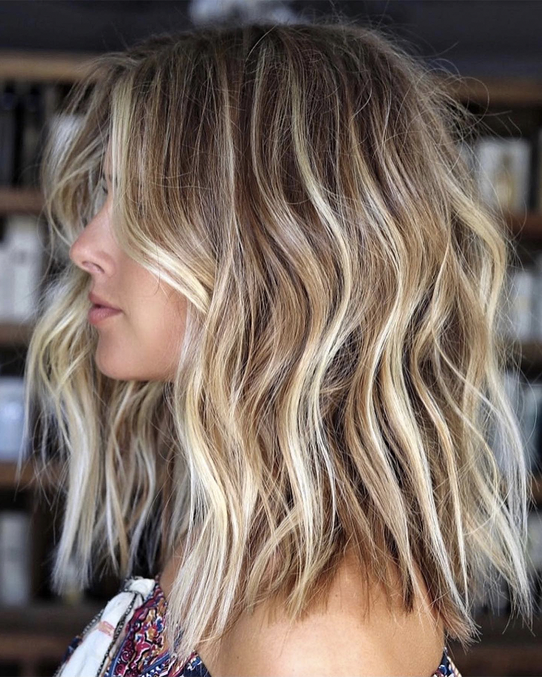 A blonde woman stands side on with hair done by Amiee Marie.