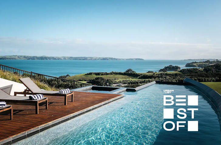 A stunning pool and row of deck chairs with stripy towels on them overlooking an incredible view of the Hauraki Gulf. 