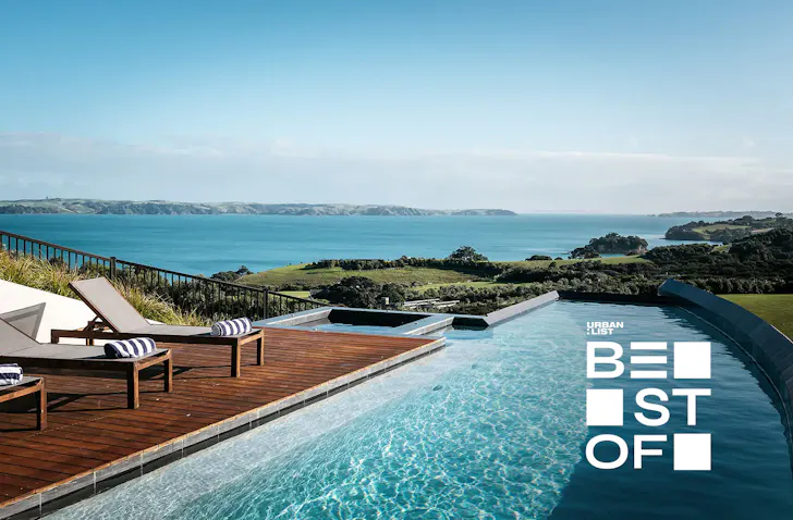 A stunning pool and row of deck chairs with stripy towels on them overlooking an incredible view of the Hauraki Gulf. 