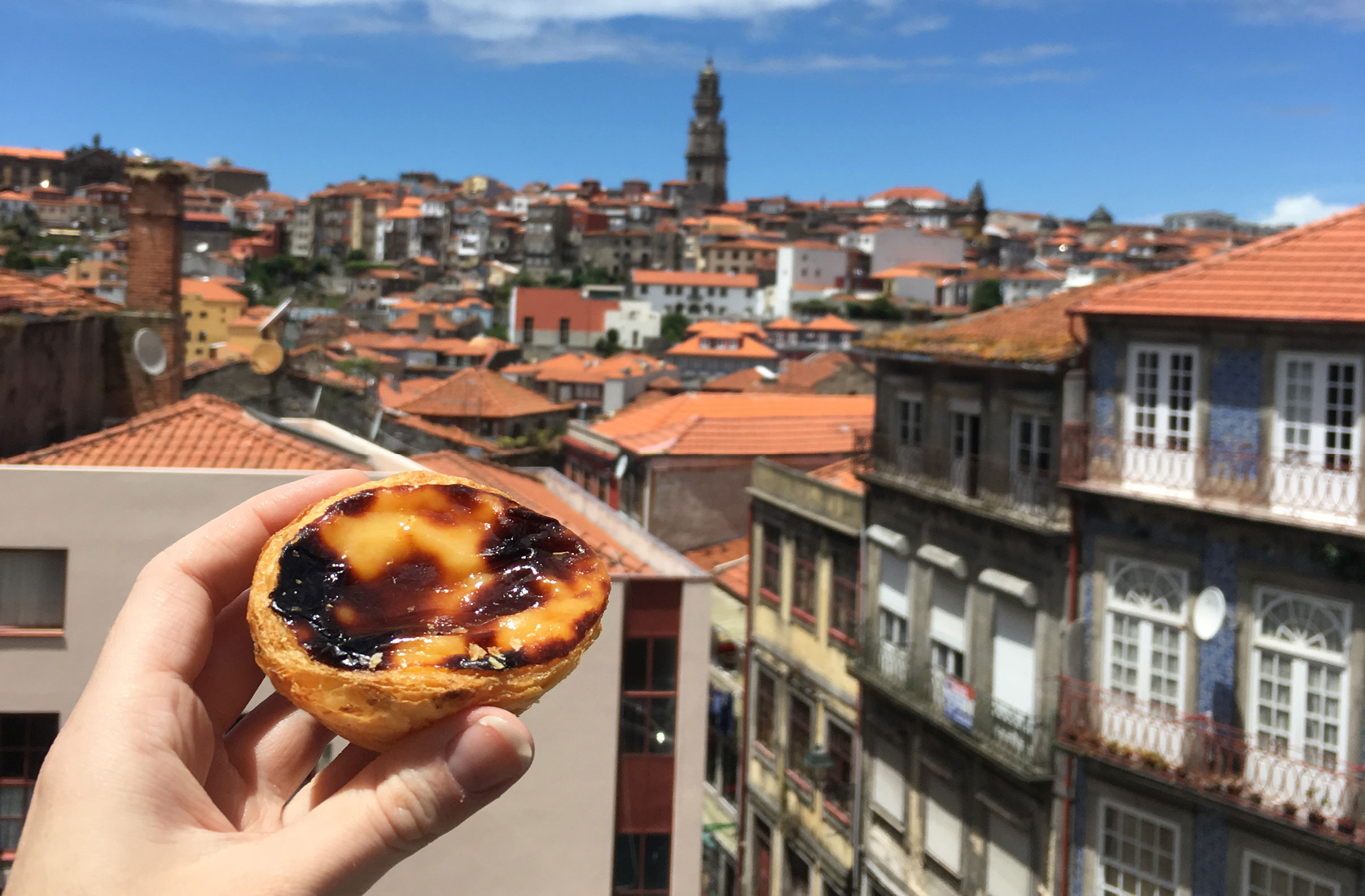 A Portuguese Pastel de Nata pastry held with Lisbon in the background 