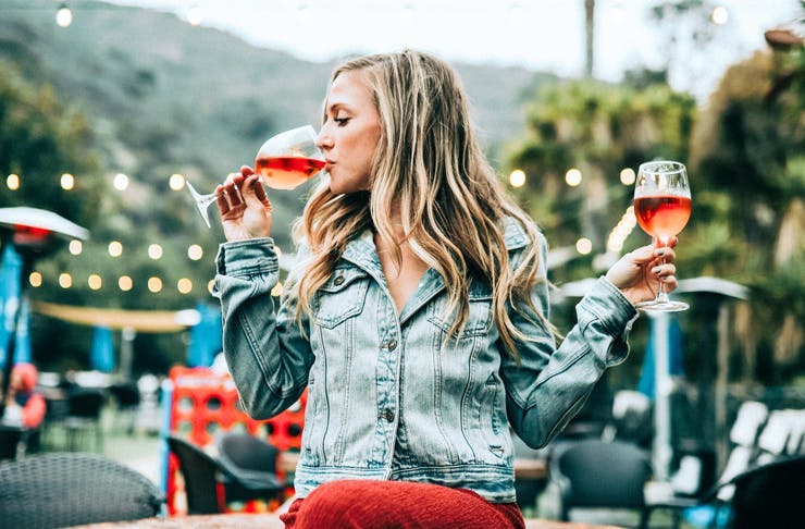 Gilr drinking one glass of wine with another glass of wine in the other hand.