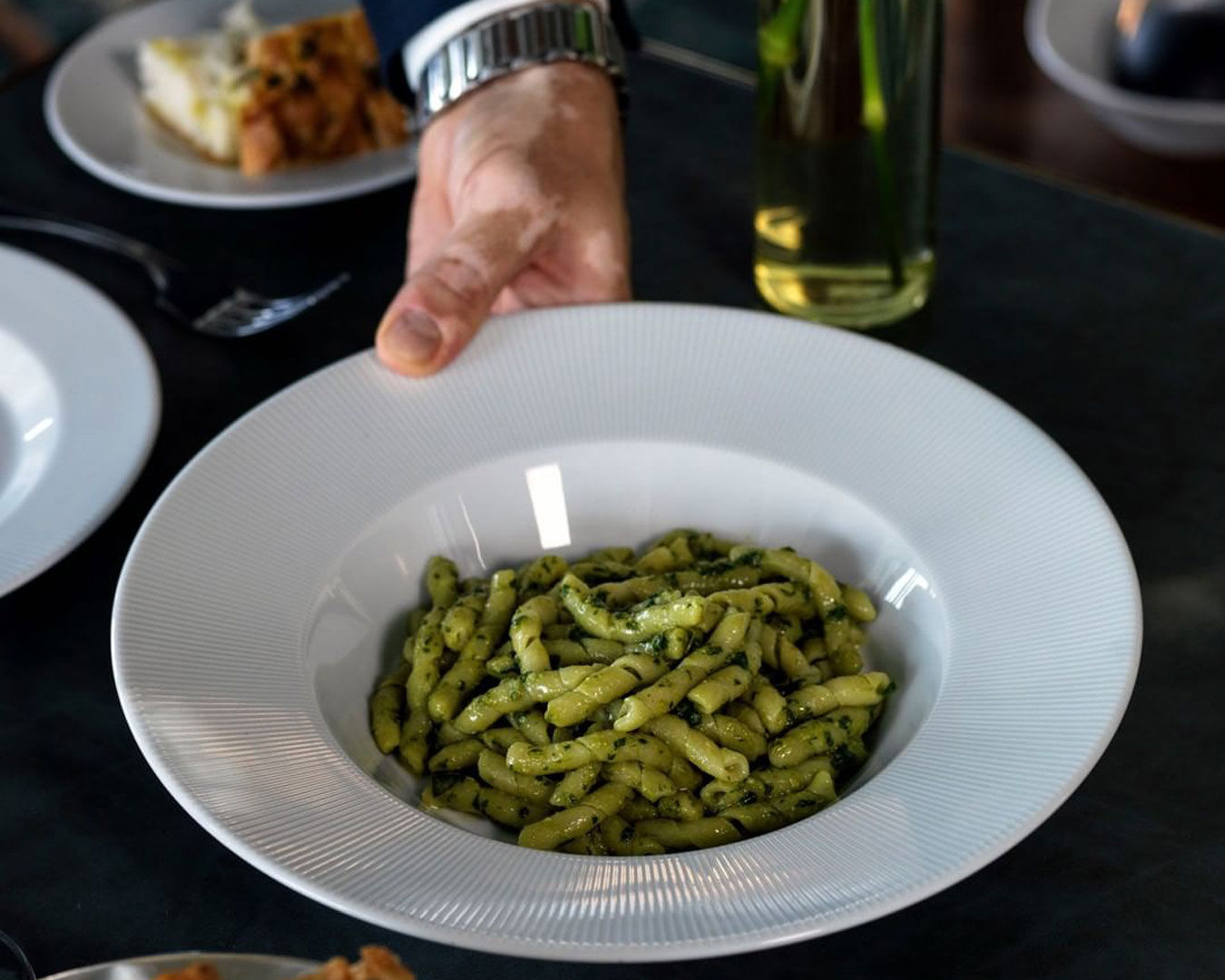 hand holding bowl of green pasta