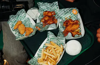 Selection of Wingstop menu items including chicken wings, boneless bites, fries and ranch dipping sauce served on a tray in the restaurant.