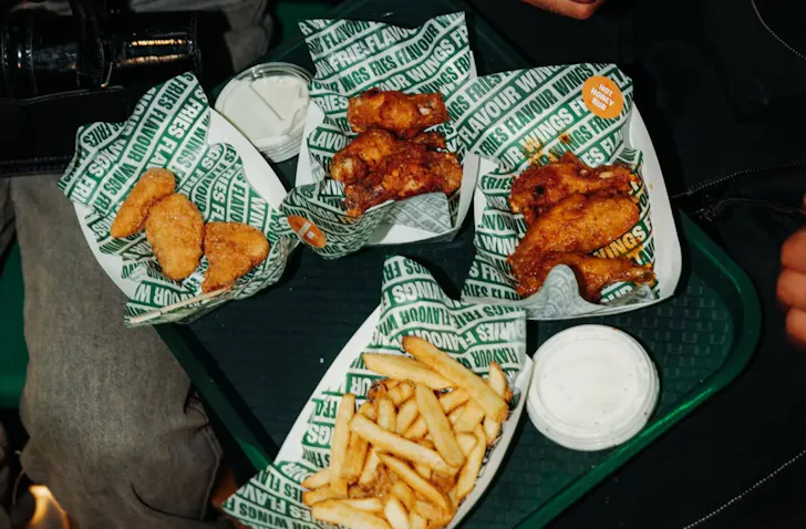 Selection of Wingstop menu items including chicken wings, boneless bites, fries and ranch dipping sauce served on a tray in the restaurant.