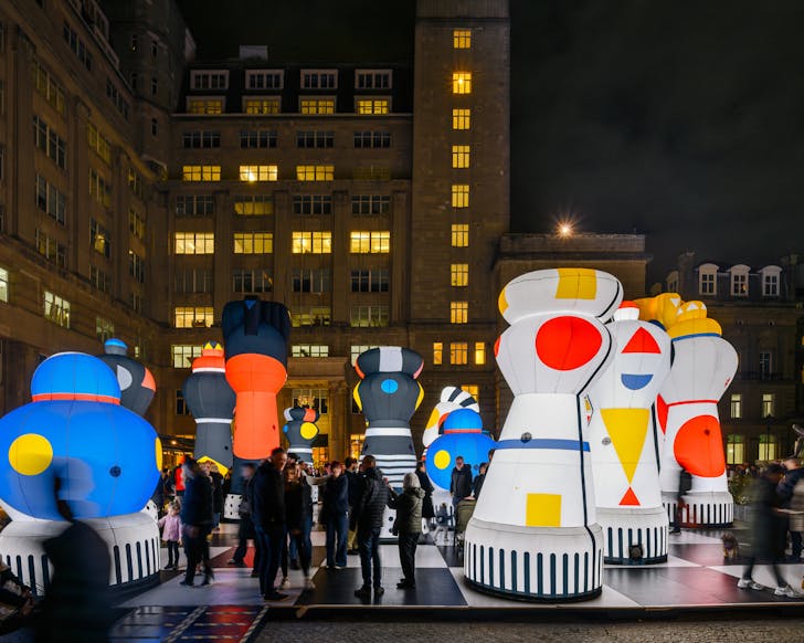 Oversized Bauhaus-inspired chess pieces tower above the crowd.